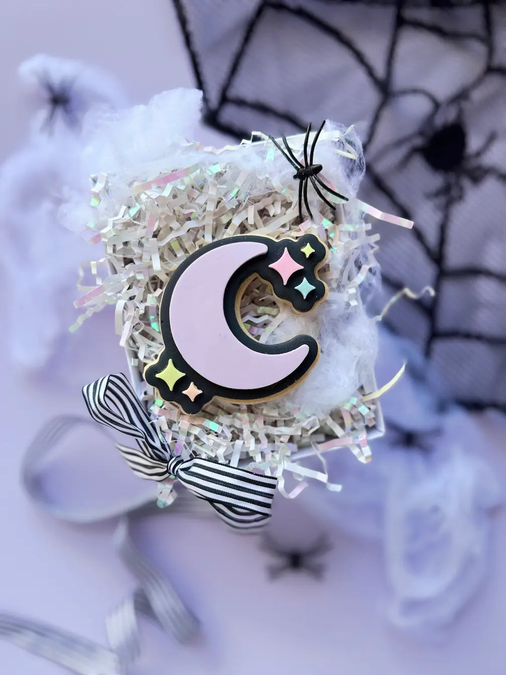 Decorated Halloween cookie shaped like a lilac crescent moon with a black outline and pastel stars.
