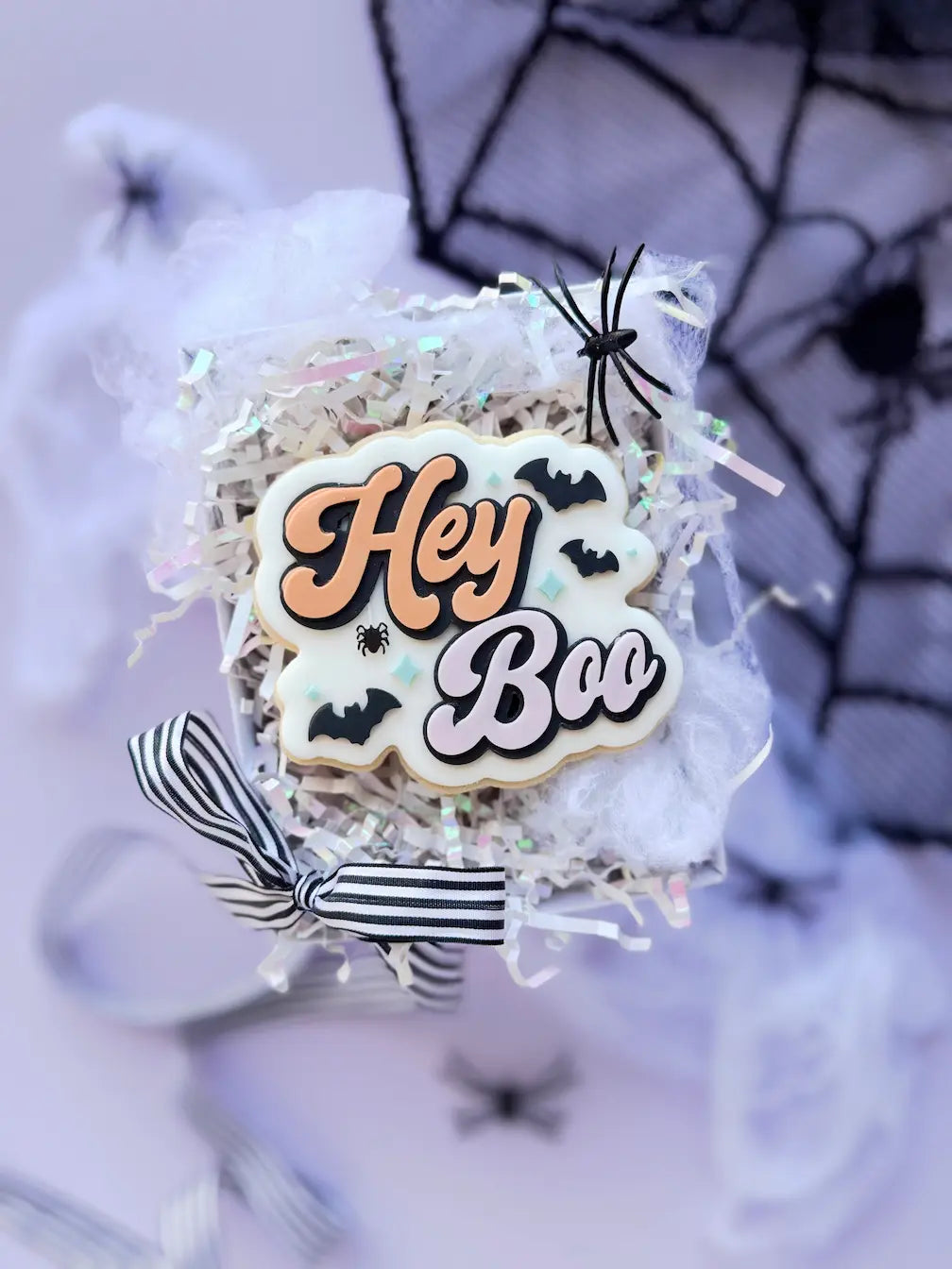 Decorated Halloween cookie with orange and lilac Hey Boo lettering, black bats and a small spider.
