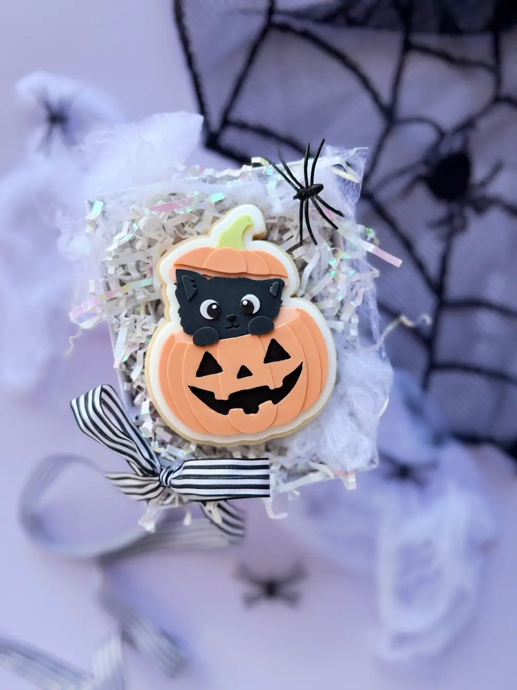 Decorated Halloween cookie with a black cat peeking out of an orange pumpkin with a carved face.