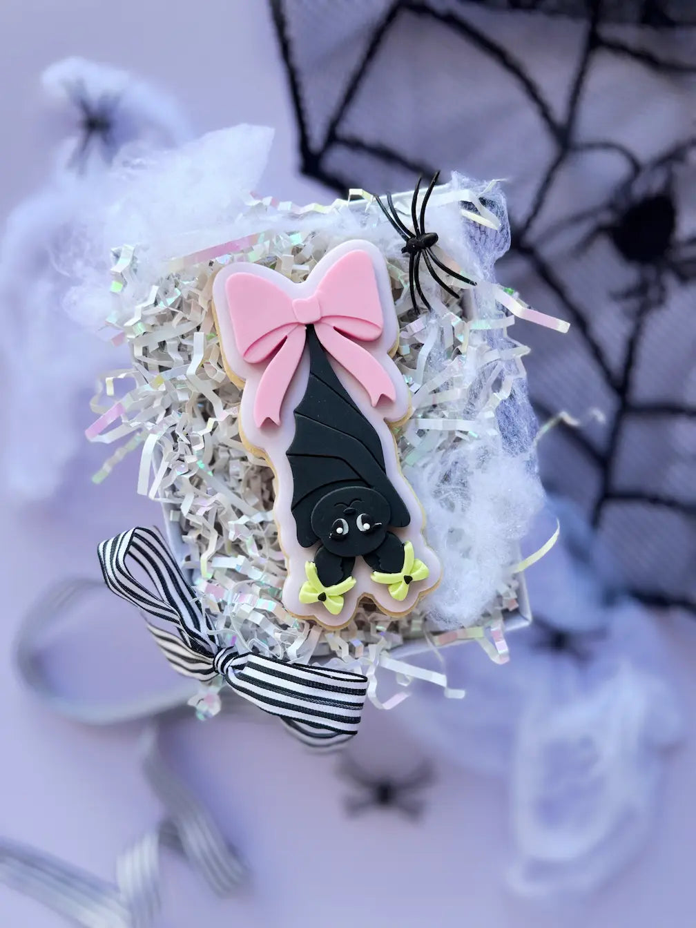 Decorated Halloween cookie with a black bat hanging upside down and a large pink bow.