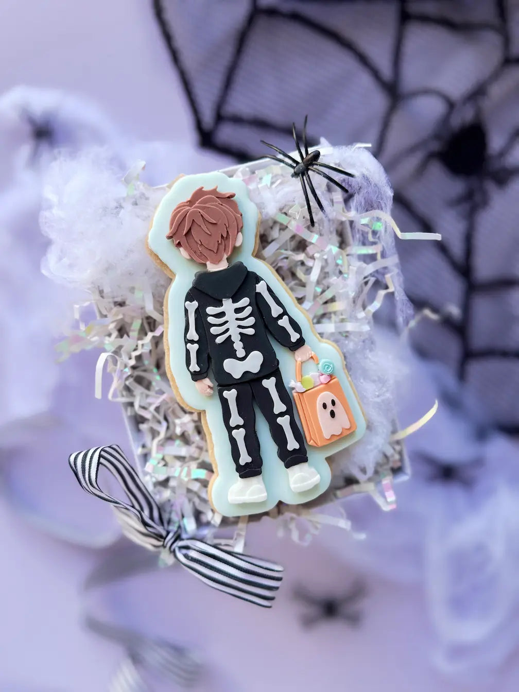 Decorated Halloween cookie showing a boy from behind in a black skeleton costume with an orange candy bag.
