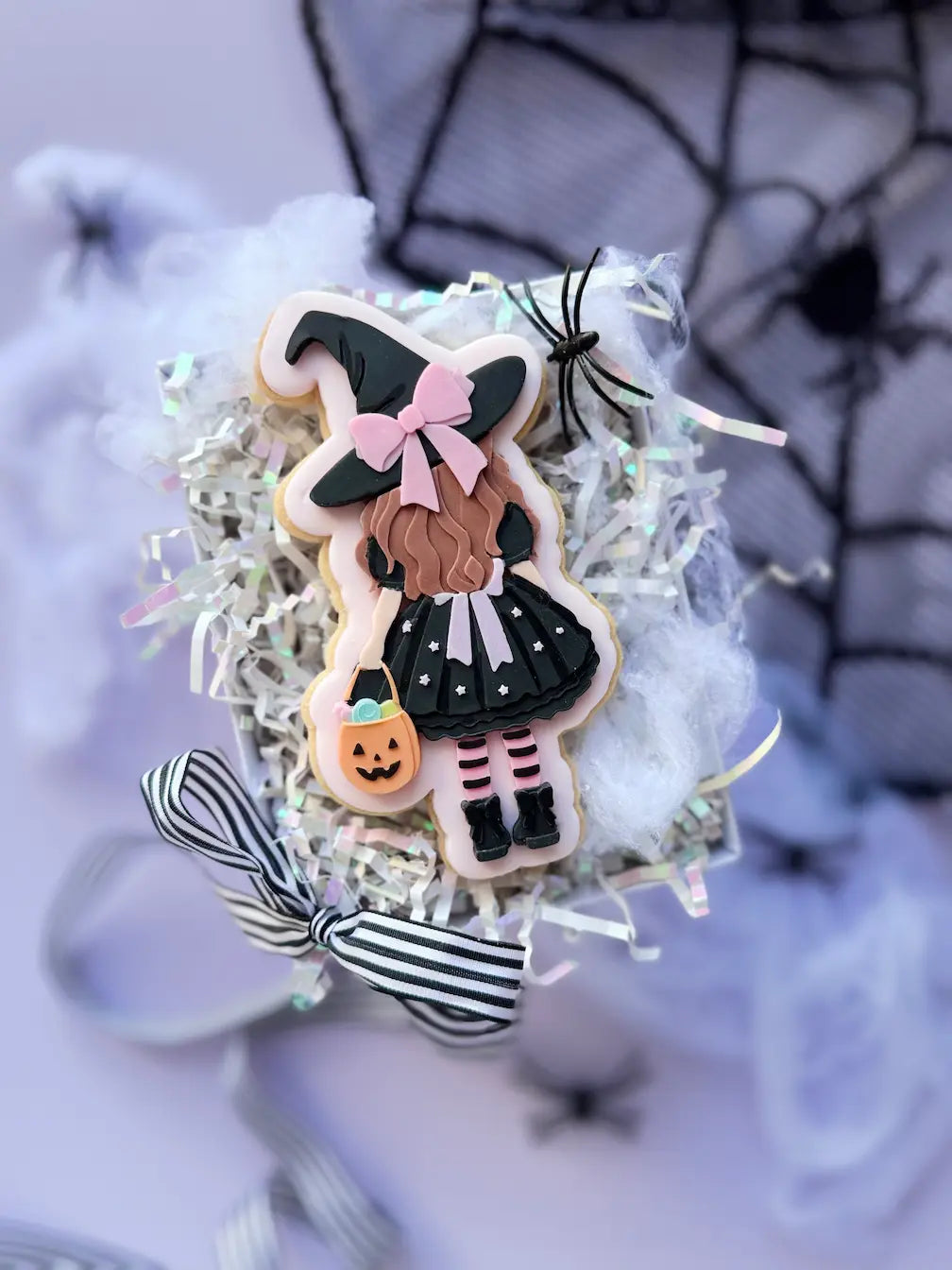 Decorated Halloween cookie showing a girl from behind with a black witch hat, a pink bow and a pumpkin bag.
