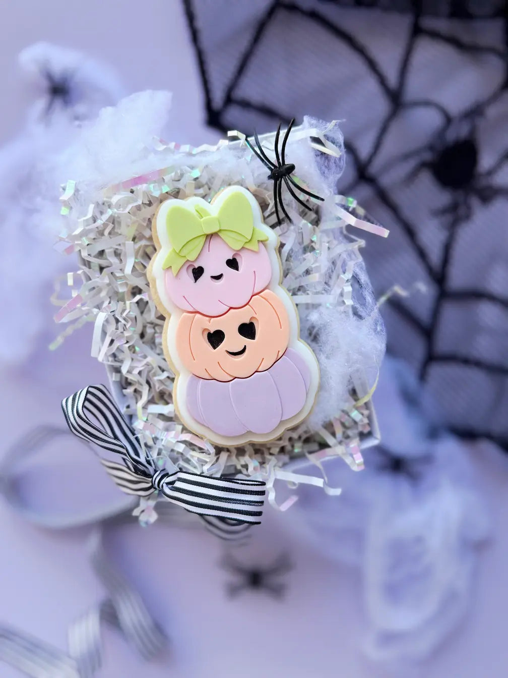 Decorated cookie shaped like a stack of three pastel pumpkins with smiling faces and a green bow.