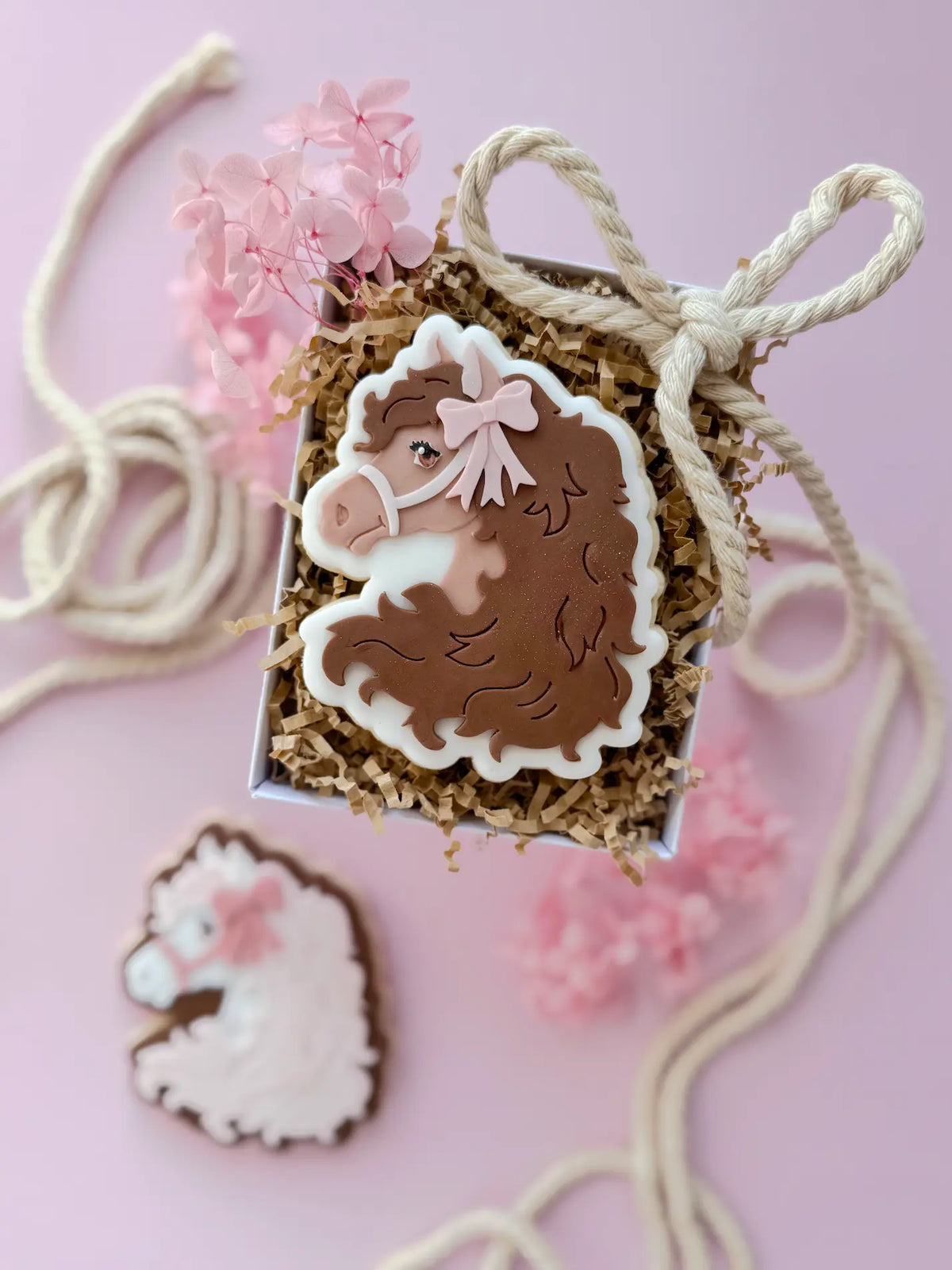 Verzierter Pferdekopf-Keks mit brauner Mähne und rosa Schleife in einer Geschenkbox.